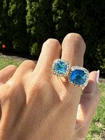 Front view of the sterling silver ring worn on a finger, showing two square-cut blue stones surrounded by clear stones.