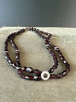 Full view of the garnet necklace laid out flat on a beige surface showing the entire necklace and clasp.
