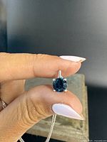 Close-up of the round London blue topaz pendant held between fingers, showing the deep blue color and silver prong setting.