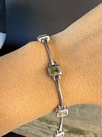 Silver multi-gemstone panel link bracelet shown on wrist, displaying rectangular bezel-set stones in green, purple, and reddish hues.