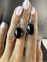Close-up photo of one black onyx and sterling silver drop earring held between fingers, showing front view and detailed texture of the earring