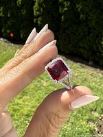 Close-up photo of a hand wearing a sterling silver ring with a large red rectangular gemstone surrounded by clear stones.