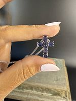Close-up of the crucifix pendant showing six oval tanzanite stones on a sterling silver base held by fingers.