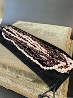 Photo showing the full view of the multi-strand necklace with alternating garnet chip and pink pearl strands laid on a black velvet pouch and beige surface.