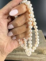 Close-up of hand holding strand of creamy white genuine pearls showing lustrous surface and round shape variations