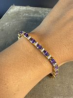 Bracelet worn on wrist showing alternating purple amethysts and clear stones in gold-overlay setting.