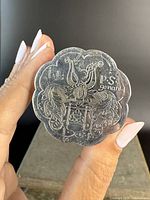 View of the engraved crest on the top surface of the lobed snuff box held between fingers against a dark background.