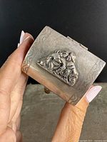 Close-up photo of the box held in hand showing embossed designs and patina.