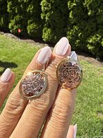 Front view of the earrings showing the detailed sun mask design with mixed metals silver and gold-tone circular background.