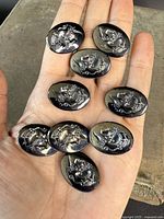 Nine carved hematite intaglios with classical profile faces in relief, shown on a palm for scale.
