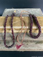 Three antique Indian garnet beaded necklaces displayed on a vintage brown velvet cushion