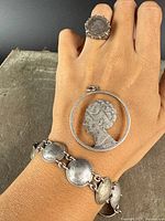 Photo showing a hand wearing a silver coin ring, the coin pendant, and the linked coin bracelet to display all three pieces together.
