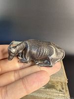 Close up of antique sterling silver cow paperweight held on fingertips showing textured details of the body and head in resting position.