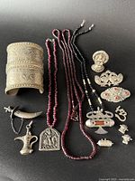 Top view of the collection showing the cuff bracelet, beaded necklaces, pendants, earrings and pins arranged on a dark background.