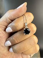 Close-up of the pendant showing the round-cut natural black diamond set in a sterling silver four-prong setting, held between fingers.