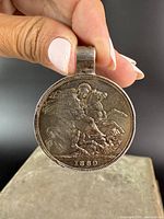 Front view of silver coin pendant showing Saint George slaying the dragon with date 1889