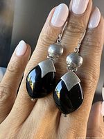 Front view of the pair of large vintage drop earrings with sterling silver and onyx held on hand, showing the textured silver bead and polished onyx teardrop pendant.