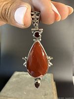 Front view showing the large pear-shaped faceted reddish gemstone with a round garnet on top and a smaller faceted stone at the bottom, set in detailed sterling silver.