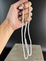 Photo of one necklace held between fingers showing the faceted clear beads and 10K yellow gold clasp.