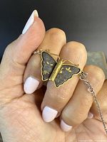 Close-up of butterfly earring showing iron inlay and gold details held by fingers