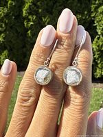 Image showing front view of sterling silver and Murano-style glass orb earrings held between fingers with natural background.
