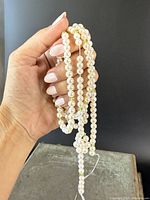 Close-up of hand holding and displaying the strand of pearls mixed with green peridot beads, showing bead detail and necklace length.