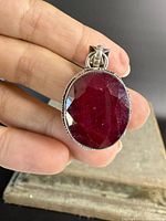 Front view of large faceted deep red ruby set in sterling silver pendant held between fingers.