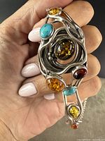 Close-up of the sterling silver cuff bracelet featuring natural amber, turquoise, and red stones in a brutalist design held in hand.