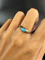 Ring worn on finger showing turquoise stone on a sterling silver band with some wear and patina.
