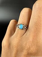 Ring worn on finger displaying the turquoise stone and silver band with intricate cut-out designs.