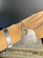 Bracelet and pendant necklace worn on wrist showing detailed engravings and overall style.