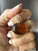 Close-up of amber pendant held in hand showing amber stone details and silver bezel