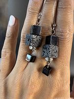 Photo of vintage MCM sterling silver and onyx cube drop earrings being worn on hand showing front view of both earrings and details of stones and silver hooks.