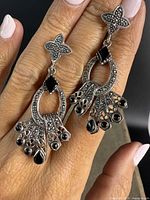 Front view of both sterling silver and marcasite drop earrings held between fingers showing detailed stones and design