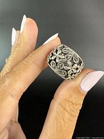 Front view of the sterling silver ring showing detailed floral and marcasite design, held between fingers.