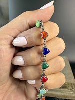 Close-up image of hand holding the sterling silver bracelet showing heart-shaped stones in green, orange, blue, red, and turquoise colours.