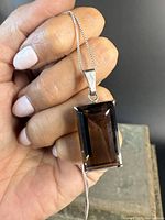 Sterling silver necklace with large rectangular smokey quartz pendant held in hand showing size and detailing.