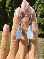 Front view of both earrings held against sunlight highlighting moonstone's glow and amethyst's purple accent.