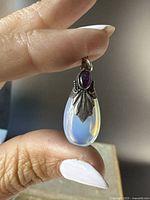 Front view of the pendant showing the glowing translucent moonstone and garnet accent set in ornate sterling silver with leaf detail.