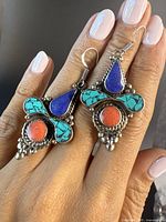 Close-up image showing the front side of the pair of large Tibetan silver earrings displaying blue lapis teardrop stones, turquoise side stones, and round coral stones with intricate silver bead detailing.