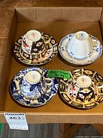 Four Royal Crown Derby cups and saucers arranged in a box showing the designs from above and the bottom stamps of the cups.