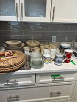 Kitchen countertop with stacks of plates, ceramic mugs, glass bowls, and woven placemats
