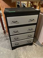Full chest of drawers showing four drawers with black frame and gray fronts, black handles, placed in storage or warehouse environment.