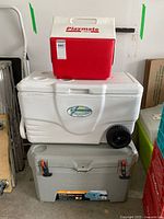 Three coolers stacked: red and white Playmate on top, white wheeled cooler in middle, gray Ozark Trail cooler on bottom