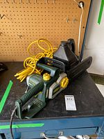 Yardworks electric chainsaw on workbench with coiled yellow extension cord attached and bottle of chain oil in the background.