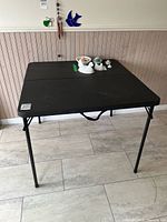 Full view of the black folding table set up indoors, showing table surface, legs, and floor beneath.