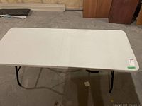 Front view of a white folding table showing the plastic top and black folding legs.