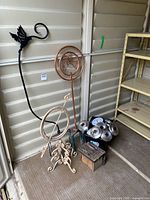 Photo of metal garden sculptures, birdhouse, solar lights grouped on floor near shelving unit.