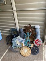 Photo showing a variety of garden decor items including Buddha statue, metal sun face, metal gecko, painted crab plate, garden signs, and decorative plaques.