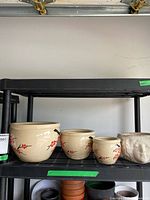 Three cream ceramic planters of different sizes with matching red floral and black bird designs, plus one child head planter